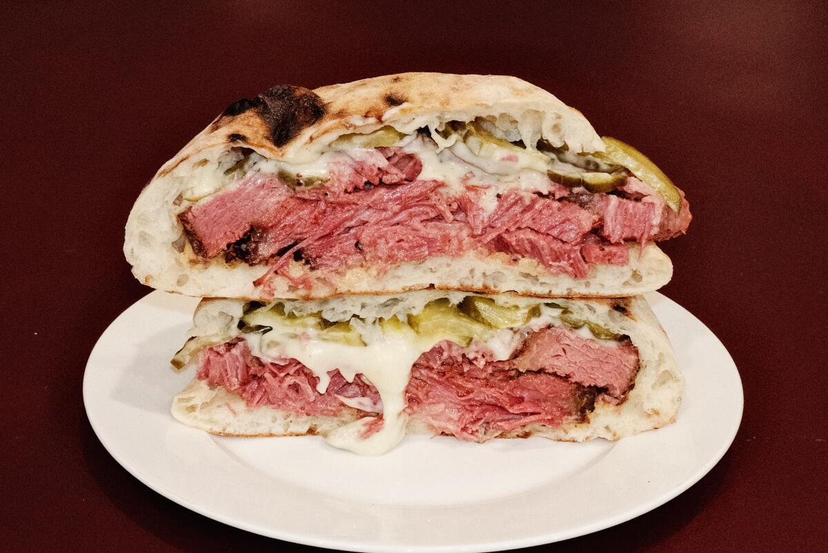 Two stacked halves of basturma brisket pita on a white plate on a red table at Yerord Mas in Glendale.