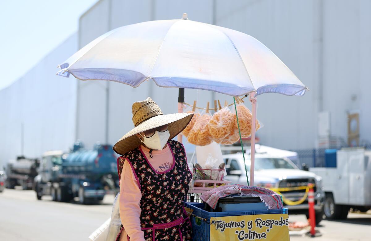 A street vendor in a straw hat pushes a food cart with an umbrella. 