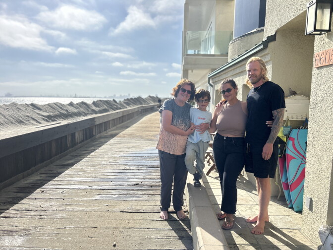 A family of four stands on a boardwalk under sunny skies.