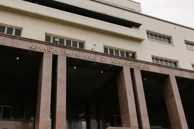 The facade and pillars of the Kenneth Hahn Hall of Administration. It's tan and light brown with gold lettering on the frame.