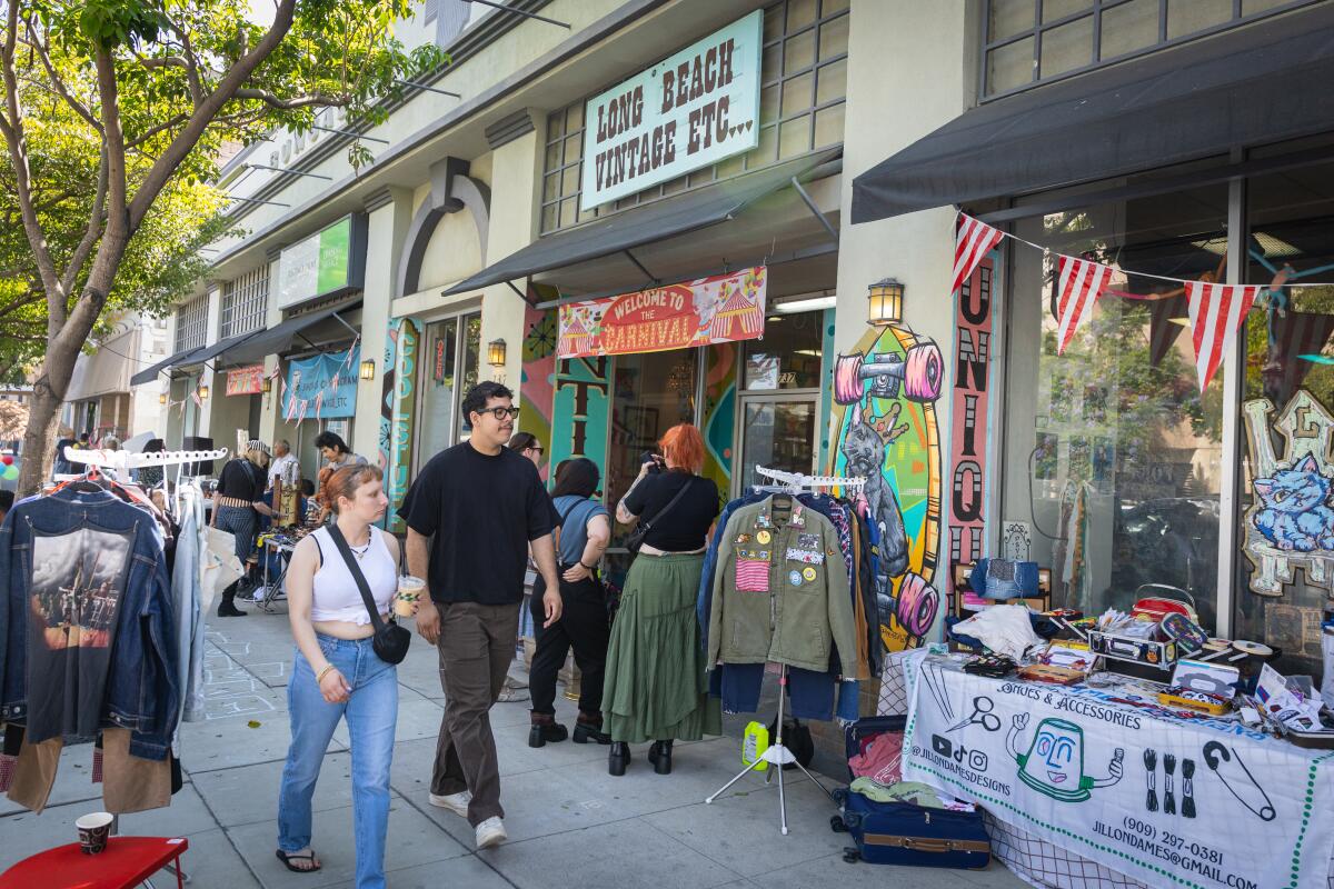 A man in a black shirt and brown pants and woman in a white tank top and blue jeans walk by a vendor selling patches.