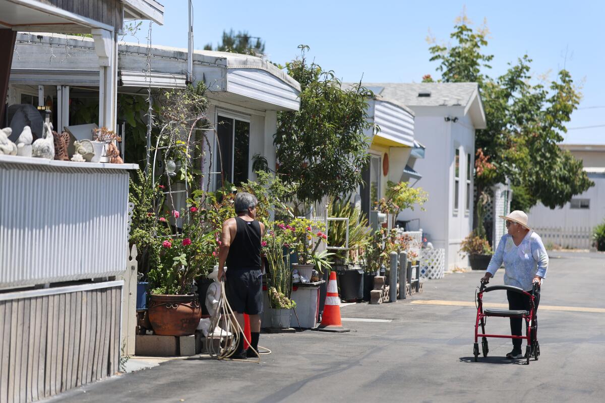 a woman who uses a walker greets her neighbor as he waters plants