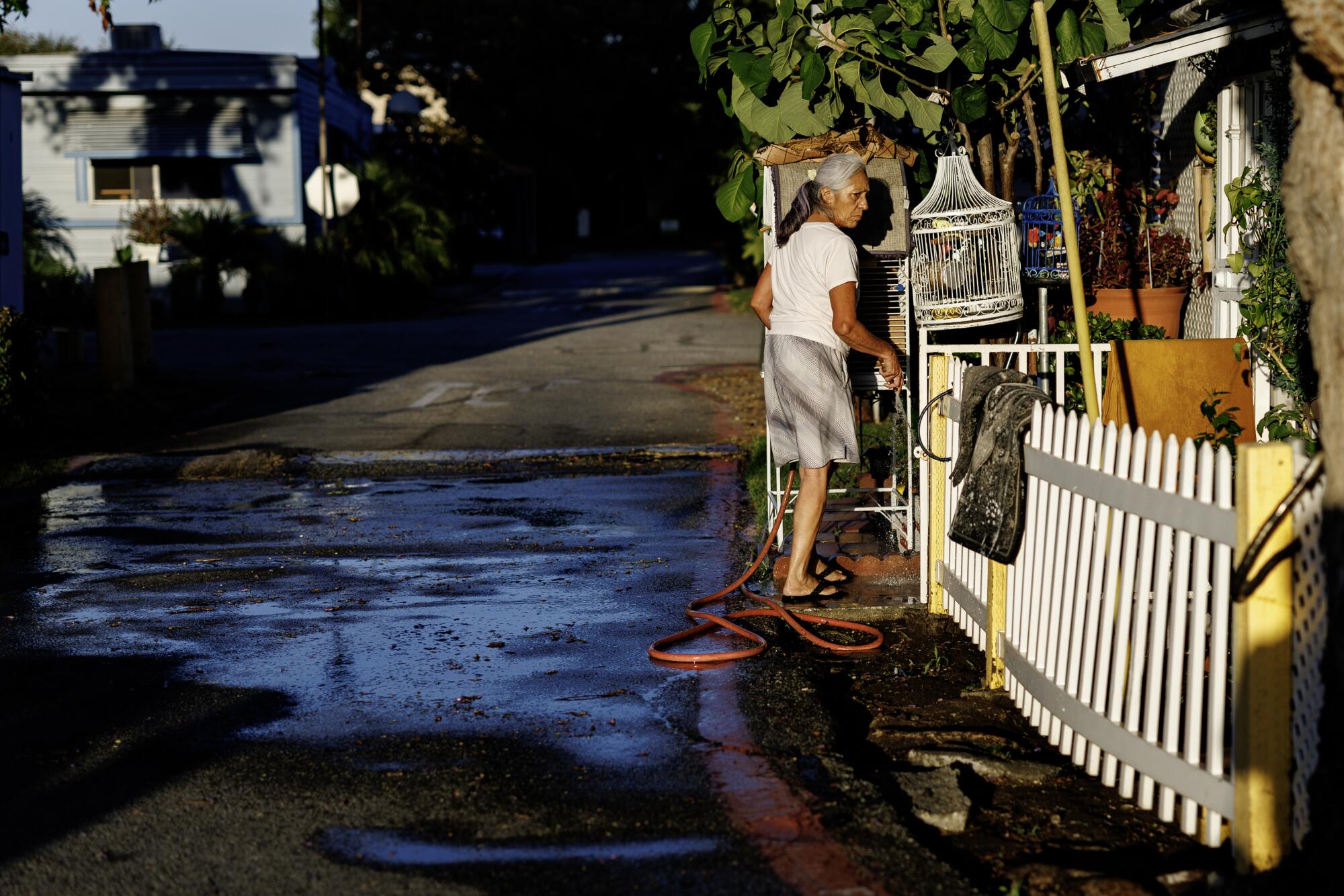 a resident waters her plants and her caged birds in front of her mobile home