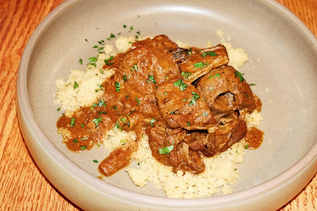 West African osso buco with tomato and coconut sauce over couscous in a tan ceramic bowl on a wood table