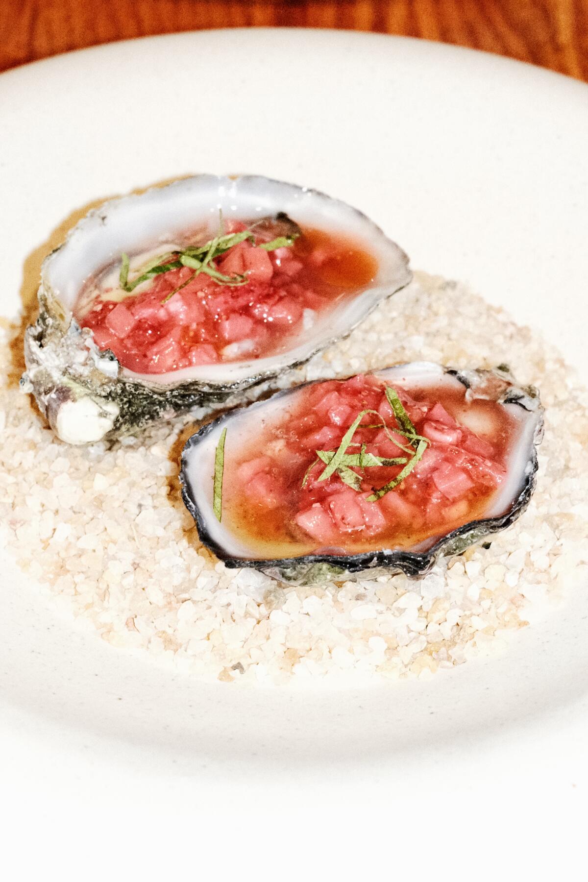 Two raw oysters with strawberry mignonette on a white plate