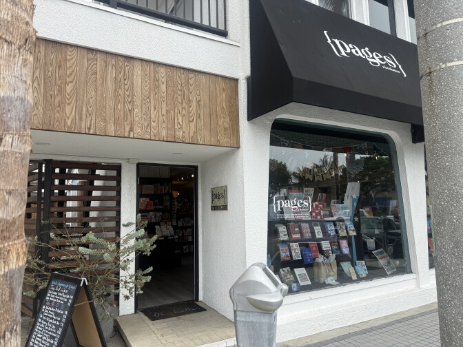 The front entrance of a bookstore is seen. An awning says "pages". The word is also seen on the glass display. There is a parking meter in the foreground of the picture.