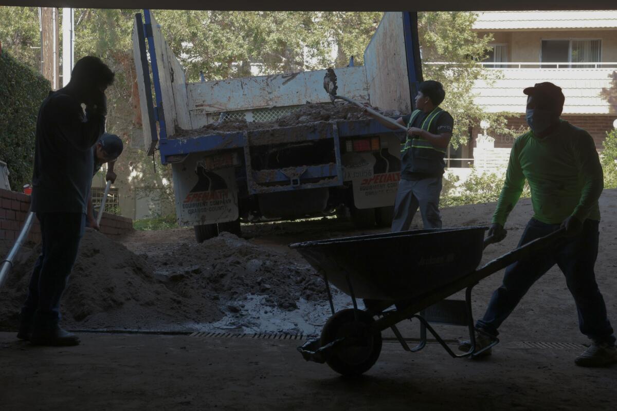 Workers shovel mud from a driveway at an apartment complex on Palm Avenue that was damaged a water main rupture.