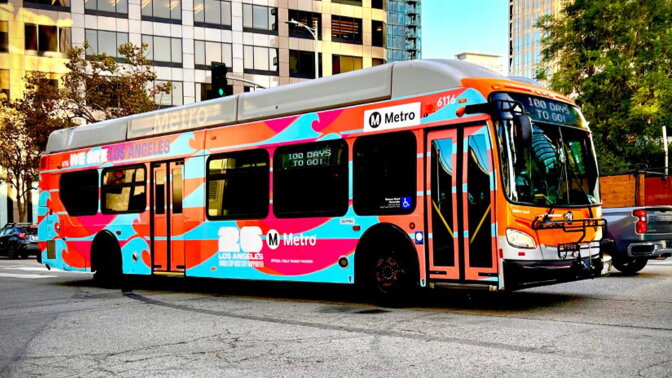 A bus is covered in a multi-colored wrap with signage that reads "26 Los Angeles World Cup" and "We are Los Angeles".