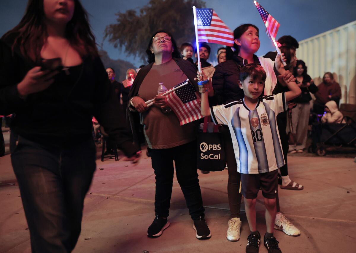 A boy wearing an Argentina jersey waves American flags as fireworks explode
