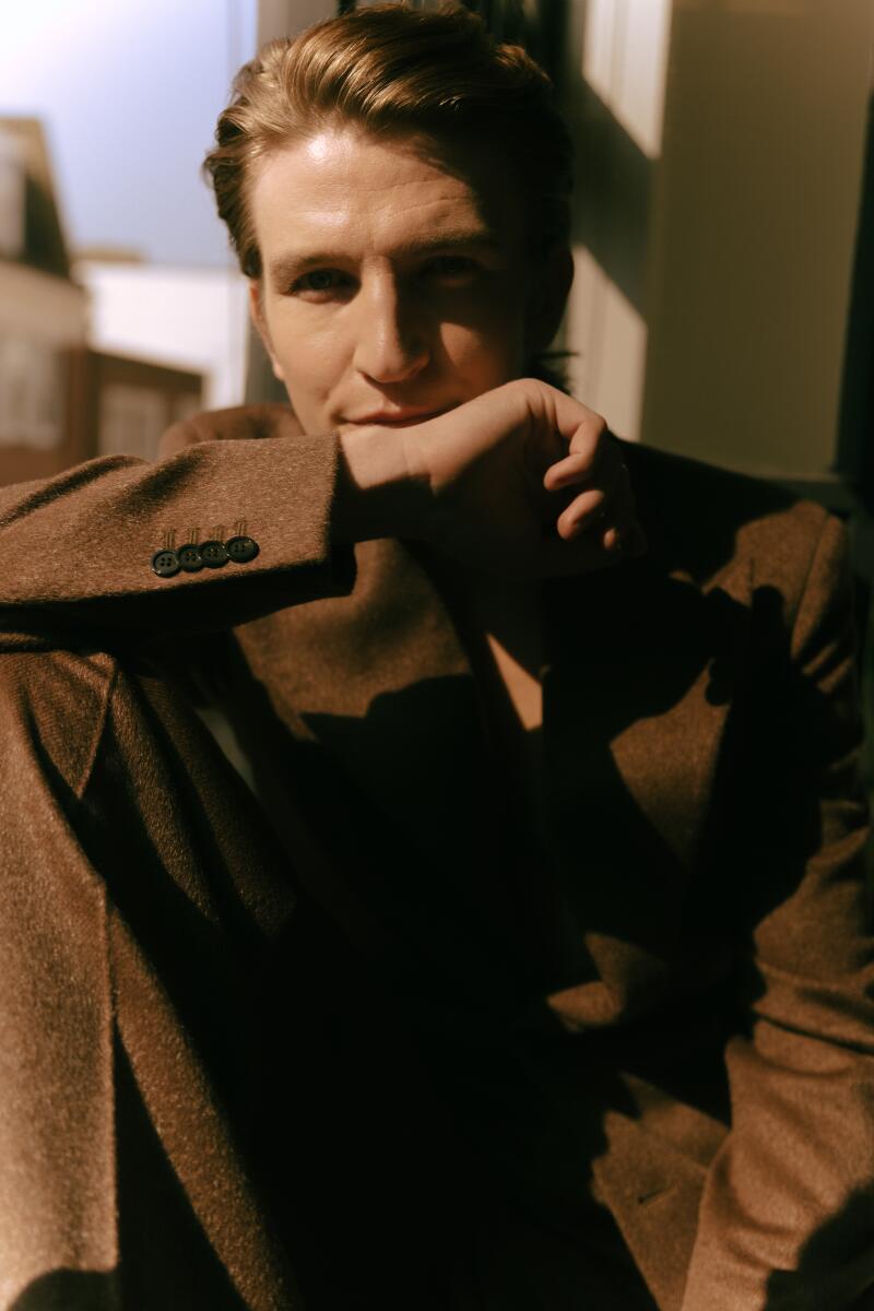 A man in a brown suit holding his hand near his mouth.