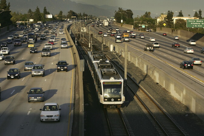 A huge multi-lane freeway full of cars is split down the middle by a Metro train and its tracks.