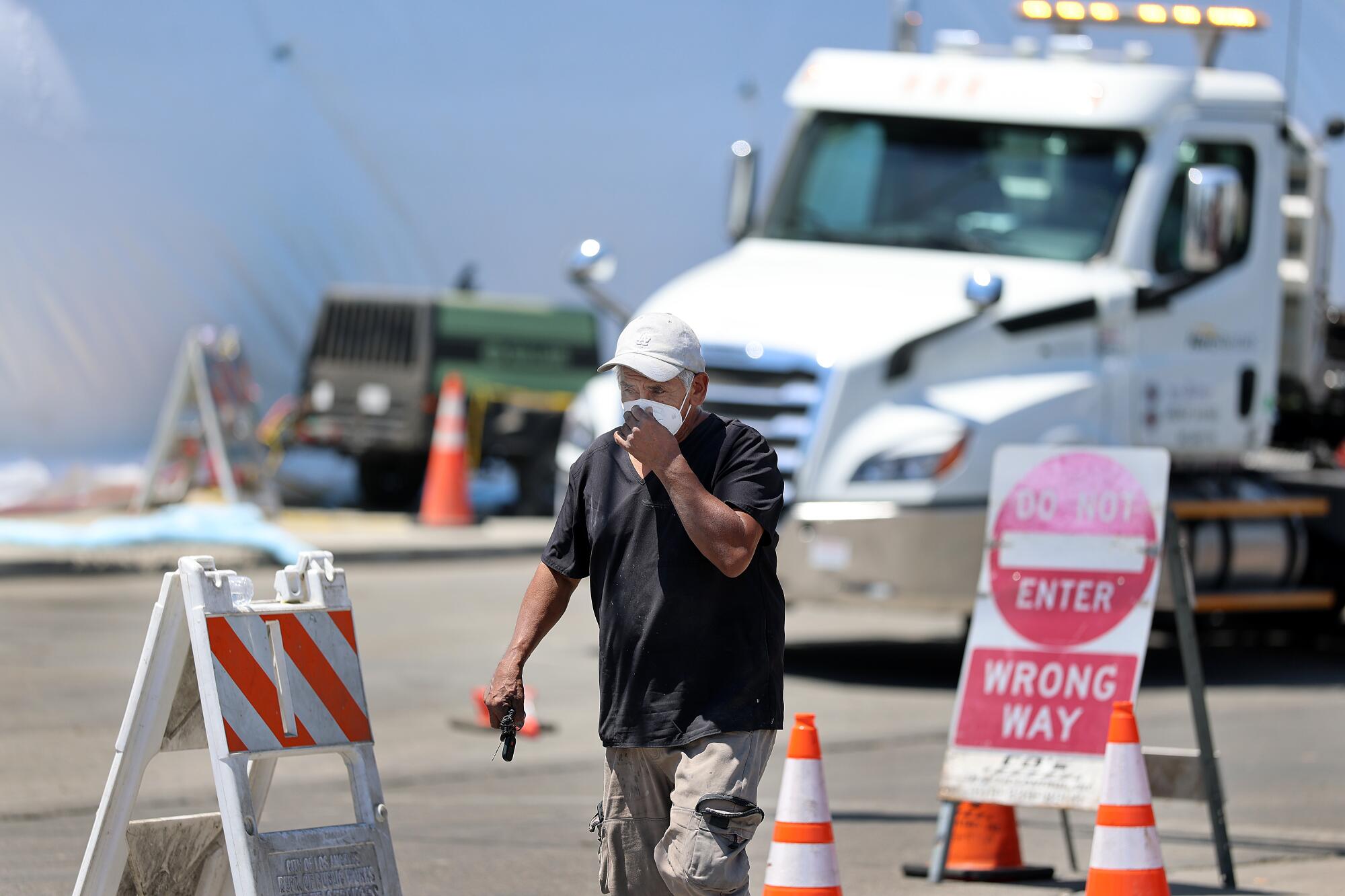 A pedestrian secures their mask as they pass by Lineage Logistics in Boyle Heights.