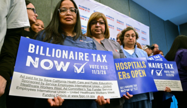 People wearing medical scrubs hold signs supporting a "Billionaire Tax" to keep hospitals and emergency rooms open, urging a vote on 11/3/26.