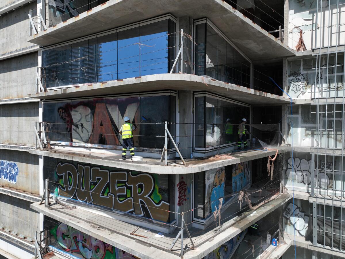 Contractors working for KPC Square LLC begin power washing and removing graffiti off the Oceanwide Plaza.