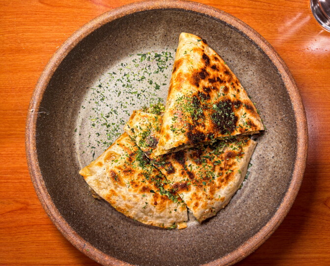The Japadilla at Homareya, a Sonoratown tortilla charred on the binchotan and dusted with aonori, cut into wedges and served in a dark ceramic bowl.