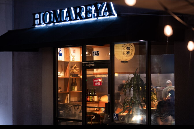 The exterior of Homareya at night, its illuminated sign glowing above a warmly lit storefront in downtown Long Beach.