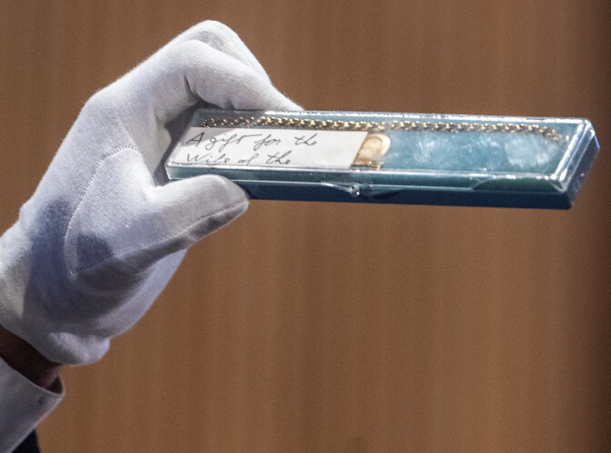 A gloved hand holds up a case containing a bracelet and white piece of paper.