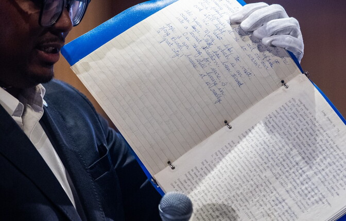 A man holds up an open, blue three ring binder with white pages with handwritten text.