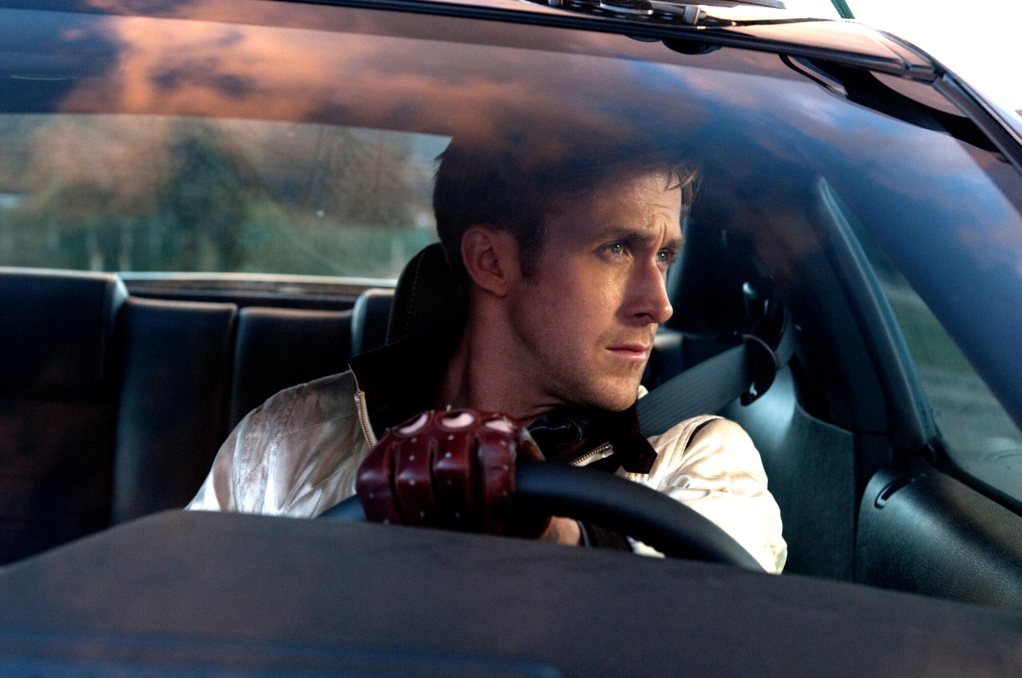 A man in a white jacket sits behind the wheel of a car.