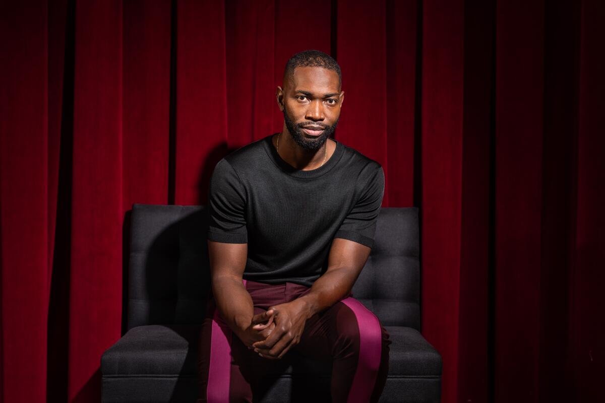 A man in a plush chair in front of a velvet curtain.