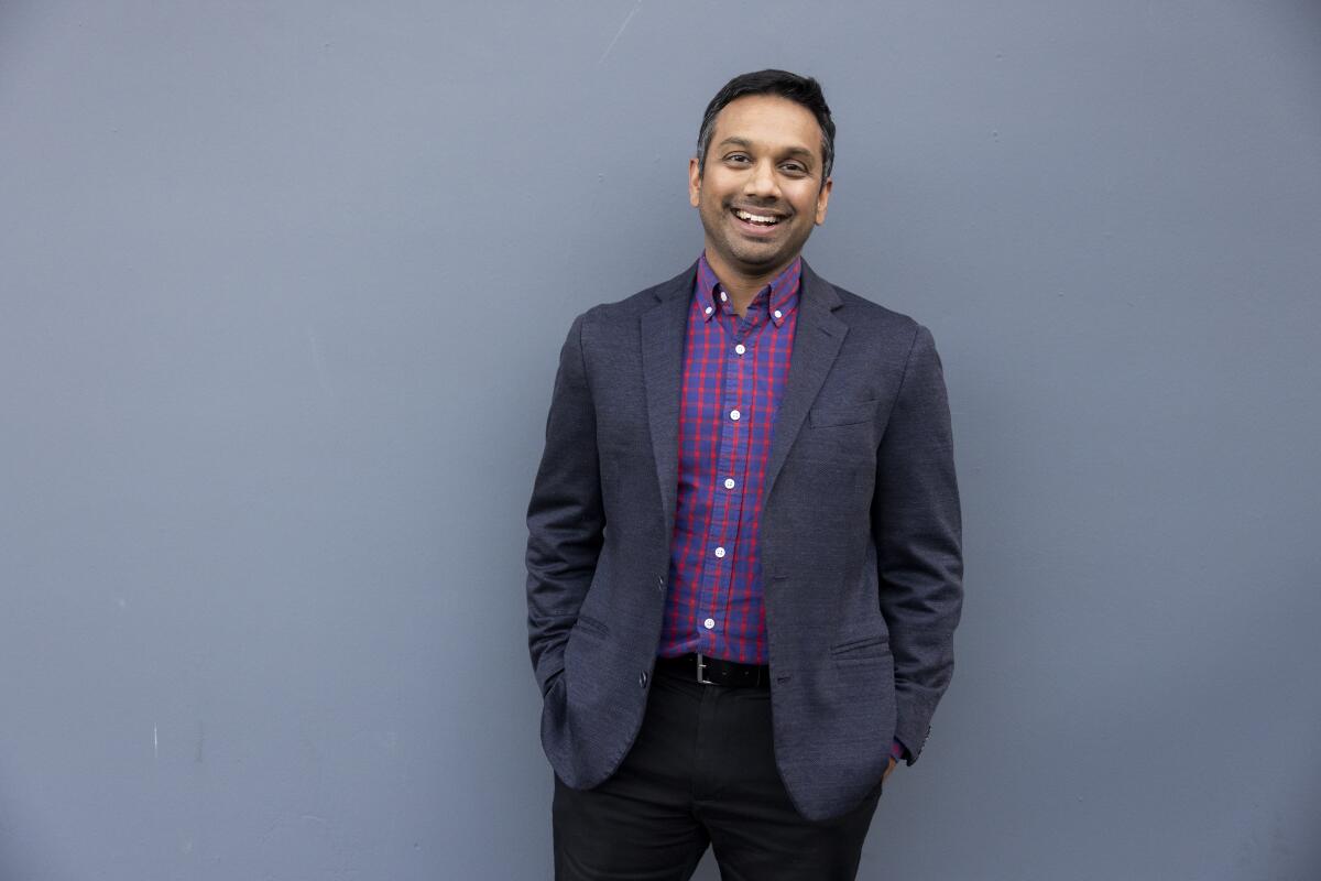 A man smiles in front of a large gray wall.