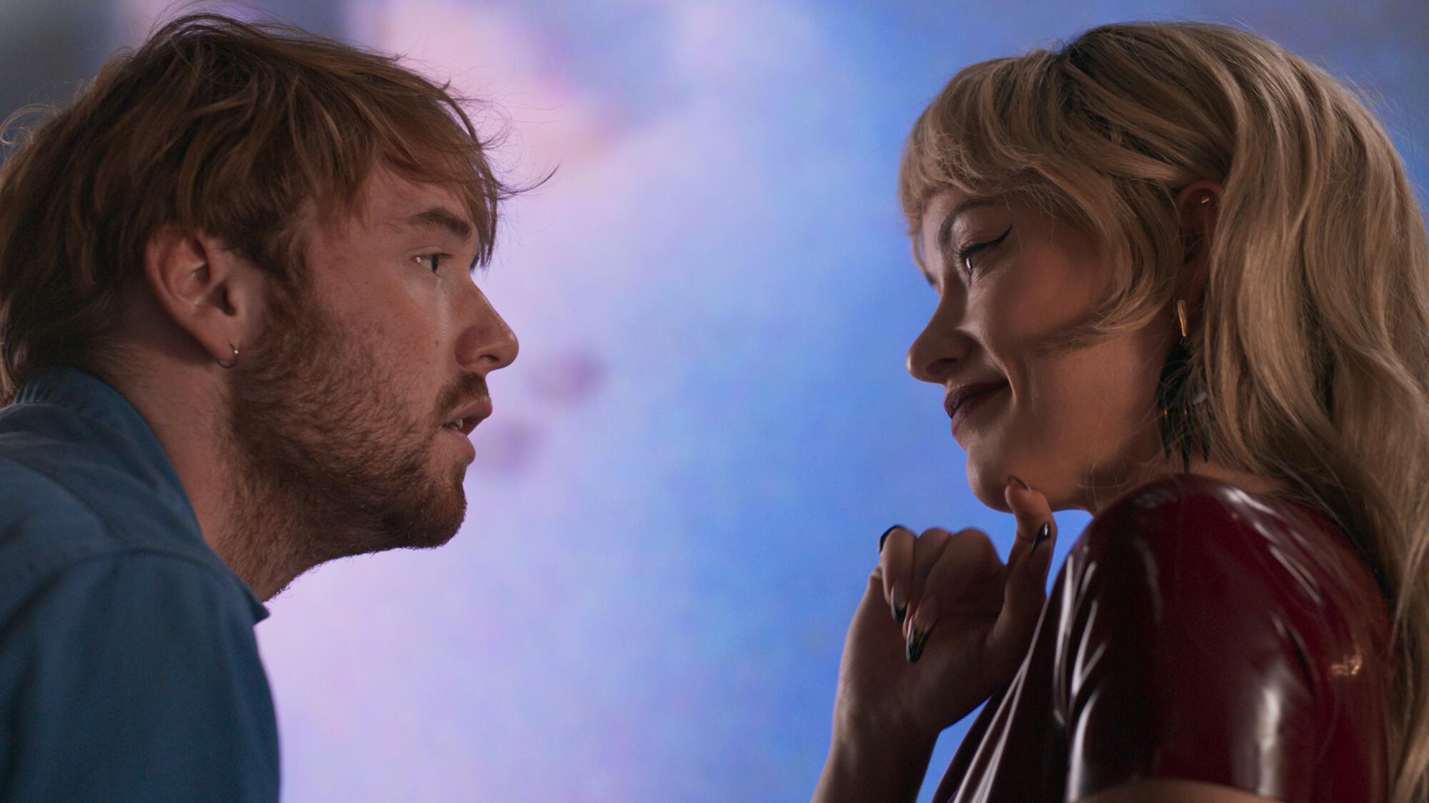 A man and a woman flirt in front of a blue and and pink background.