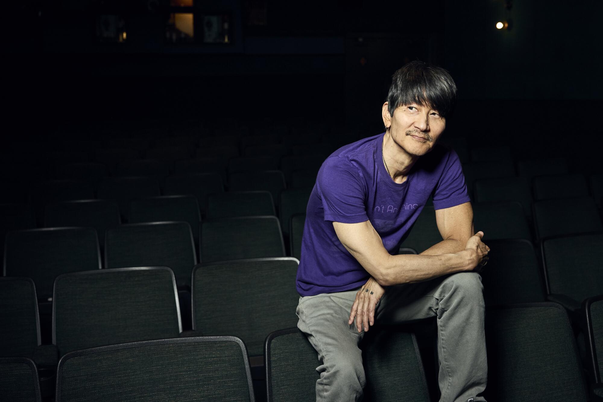 A man in a purple shirt sits in an empty theater.