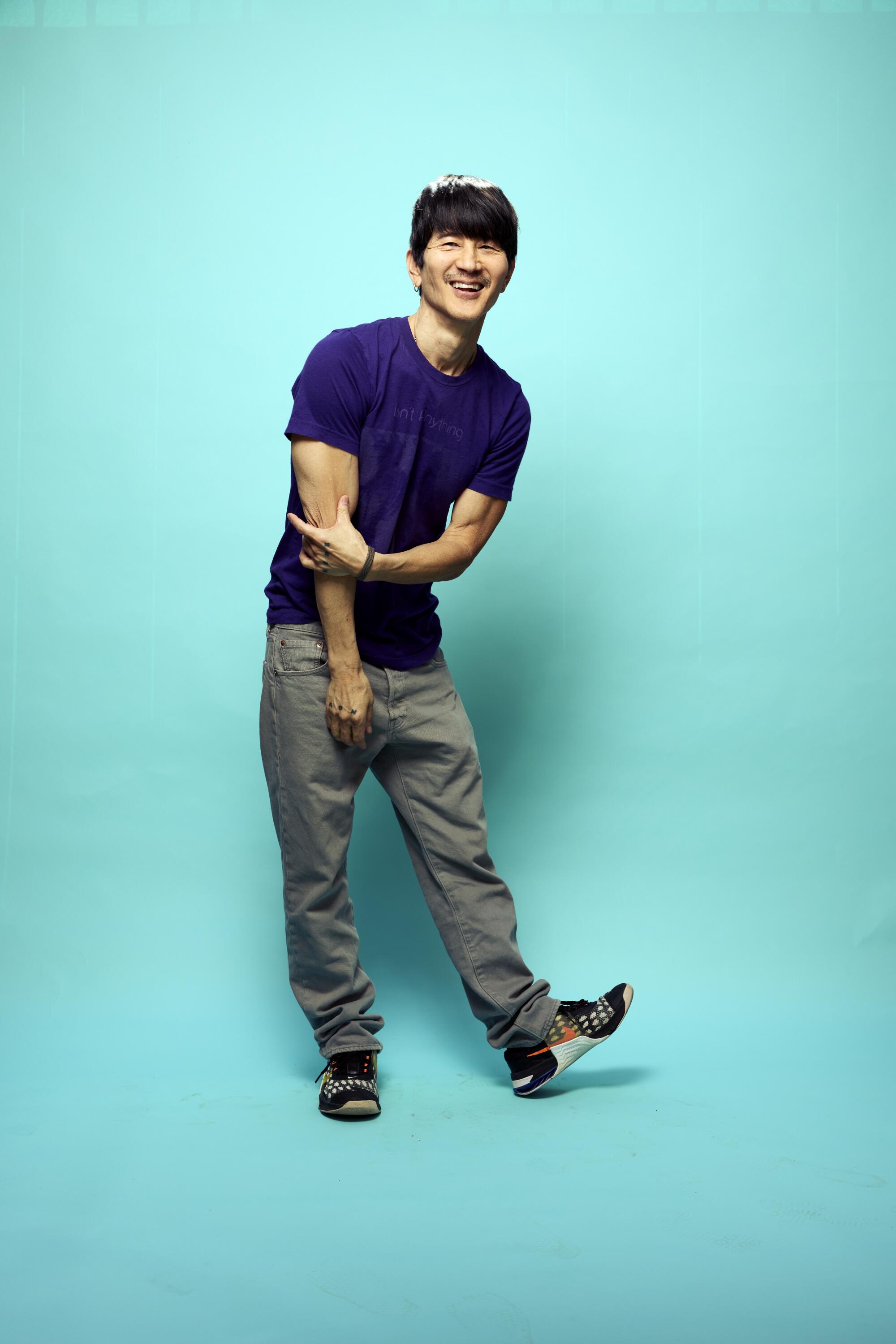 A man in a purple shirt poses in front of a light blue backdrop.