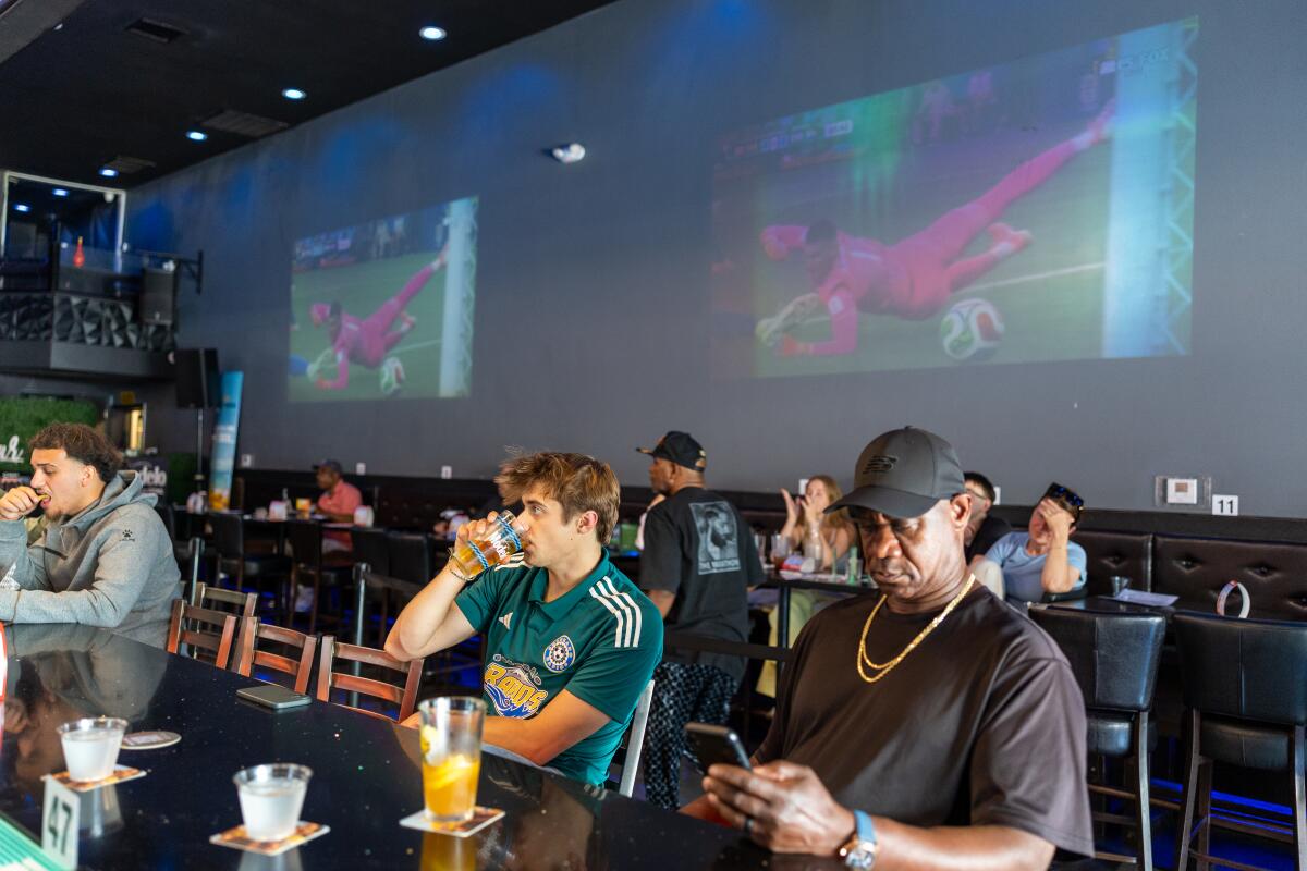 A man drinks while sitting at a bar, surrounded by other bar patrons