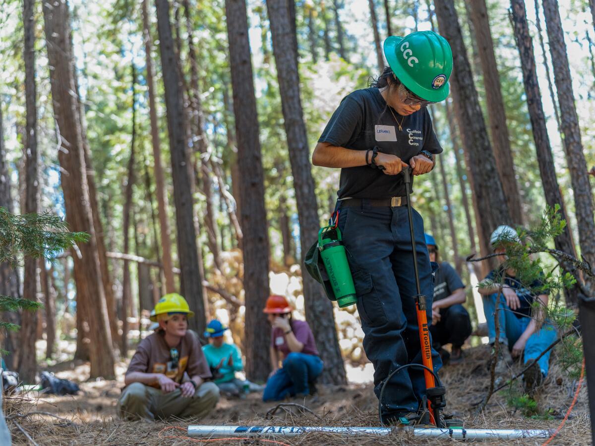 A woman in a hard hat uses a tool plunged into the ground. 