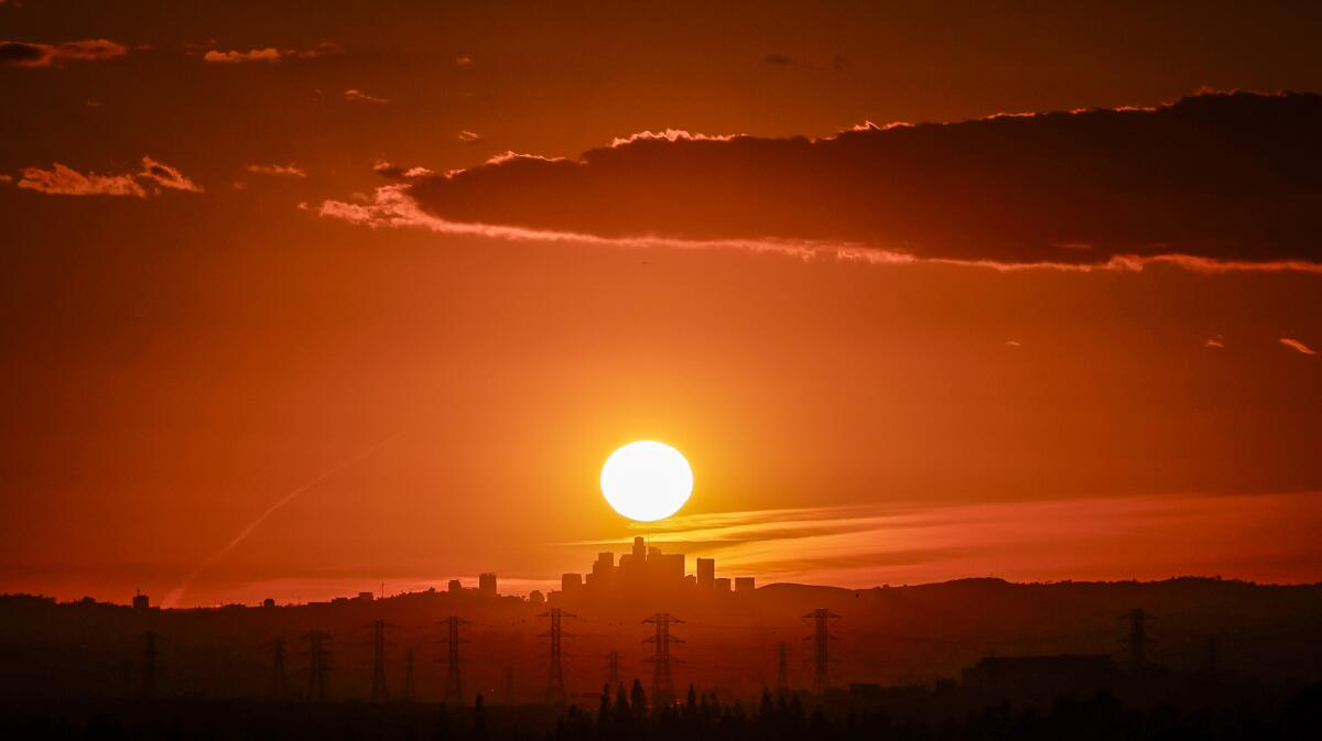 The sun sets behind the LA skyline as seen from Azusa