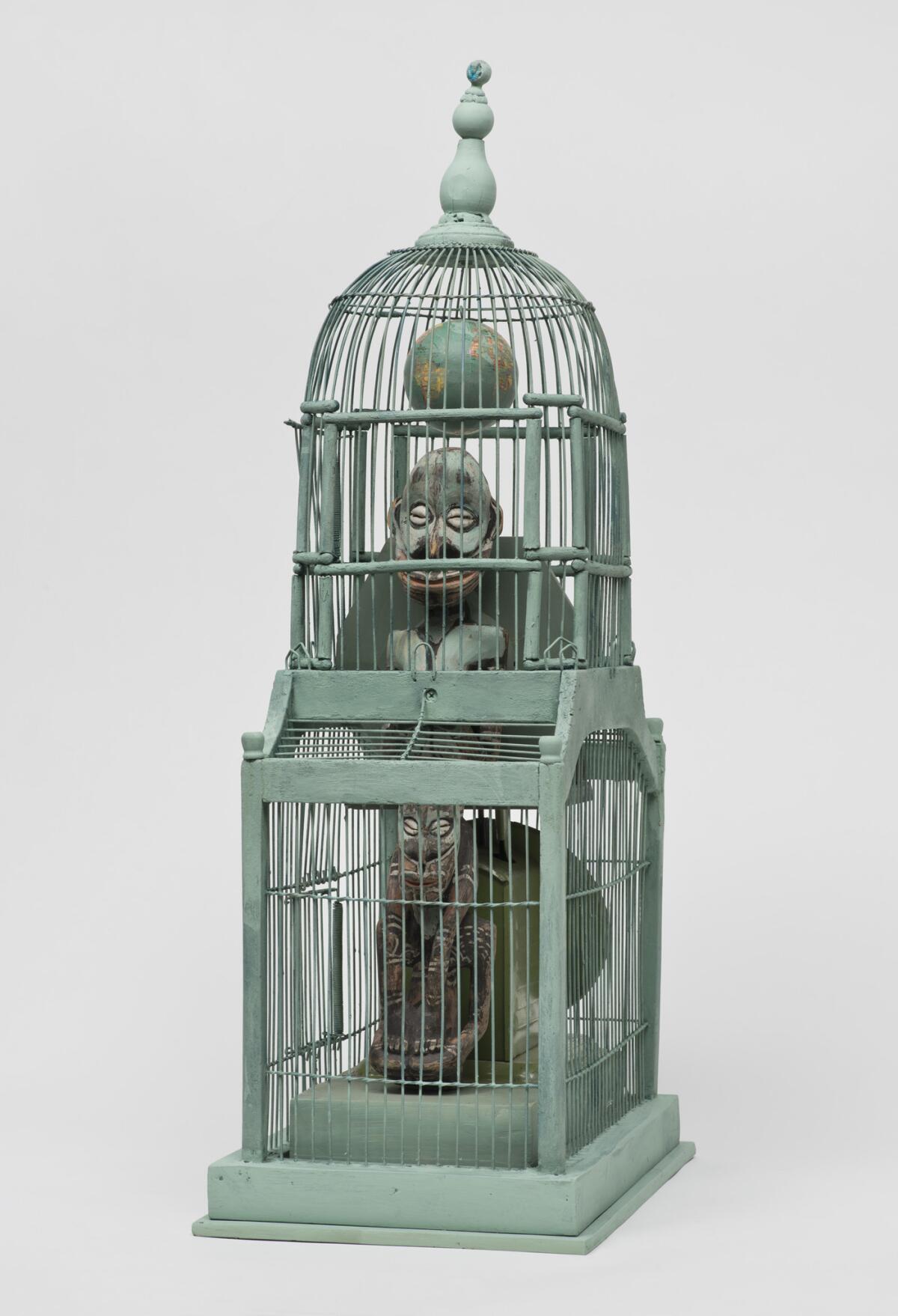 An assemblage features trapped figures inside a vintage bird cage.
