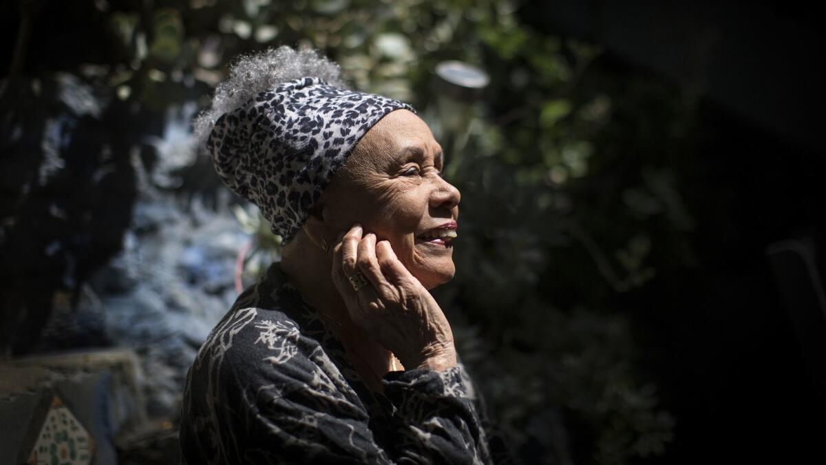 Betye Saar seen in profile and smiling ebulliently as the sun hits her face.