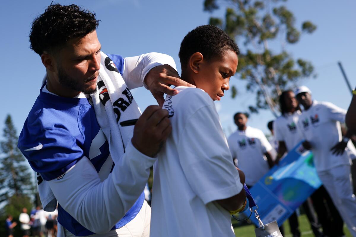 Rams running back Blake Corum, left, signs a t-shirt during an L.A. Olympics ticket donation ceremony.