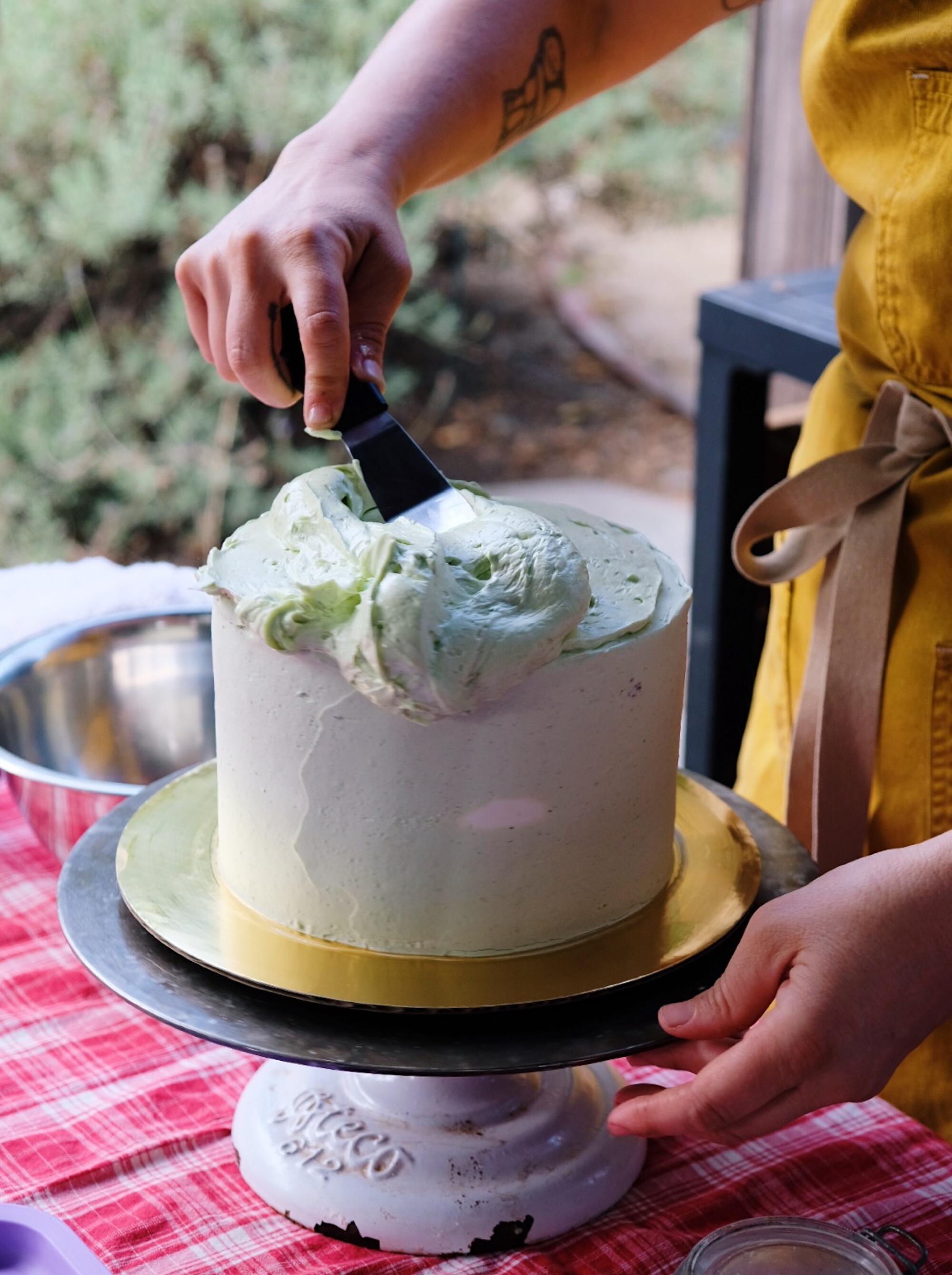 Rose Wilde spreads tomato leaf buttercream on top of a three-layer cake, using a cake turntable.