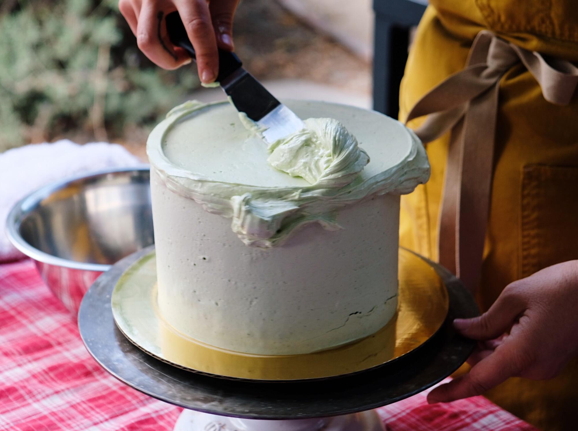 Rose Wilde uses her offset spatula to spread buttercream on top of a cake during a cake decorating workshop in her backyard.