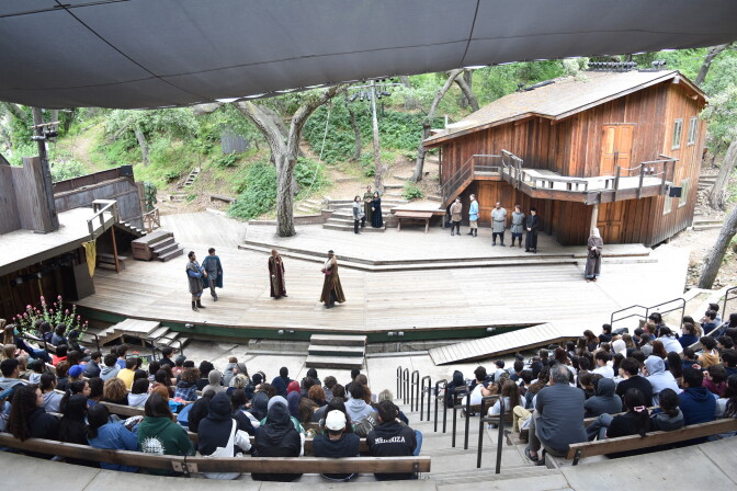 A large wooden amphitheater with 17 people onstage, and a crowd watching in the stands. 
