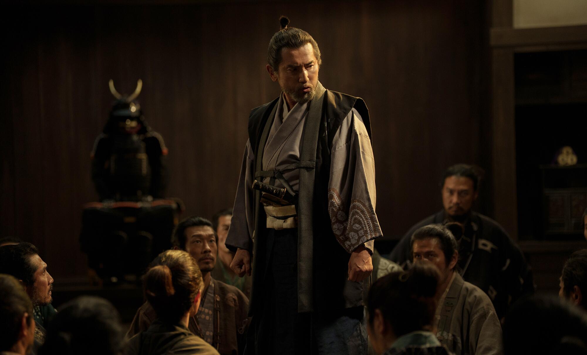 A samurai master stands among kneeling subjects.