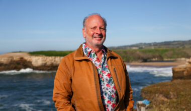 Mike Beck in a floral shirt and rust jacket by the Monterey Bay coastline.