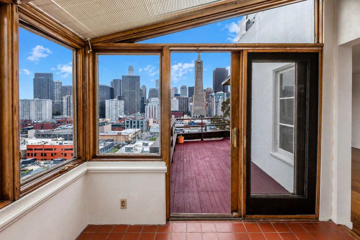 Room with large windows and a view of a city skyline, featuring skyscrapers and a red-painted outdoor deck.