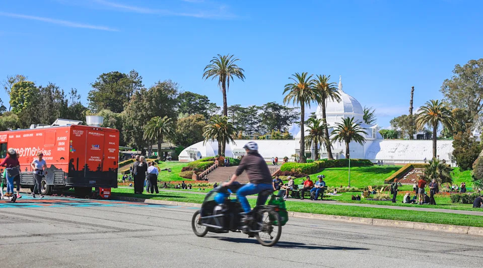 People cycling, walking, and relaxing in Golden Gate Park in front of the Conservatory of Flowers