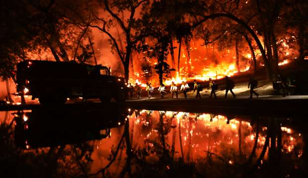 Reflected in a homeowners pool, a California Conservation Corps firefighting hand crew heads toward the Pickett Fire line, Saturday, August 24, 2025. (Kent Porter / The Press Democrat)