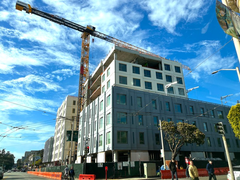 A construction crane towers over a multistory apartment project on a street corner.