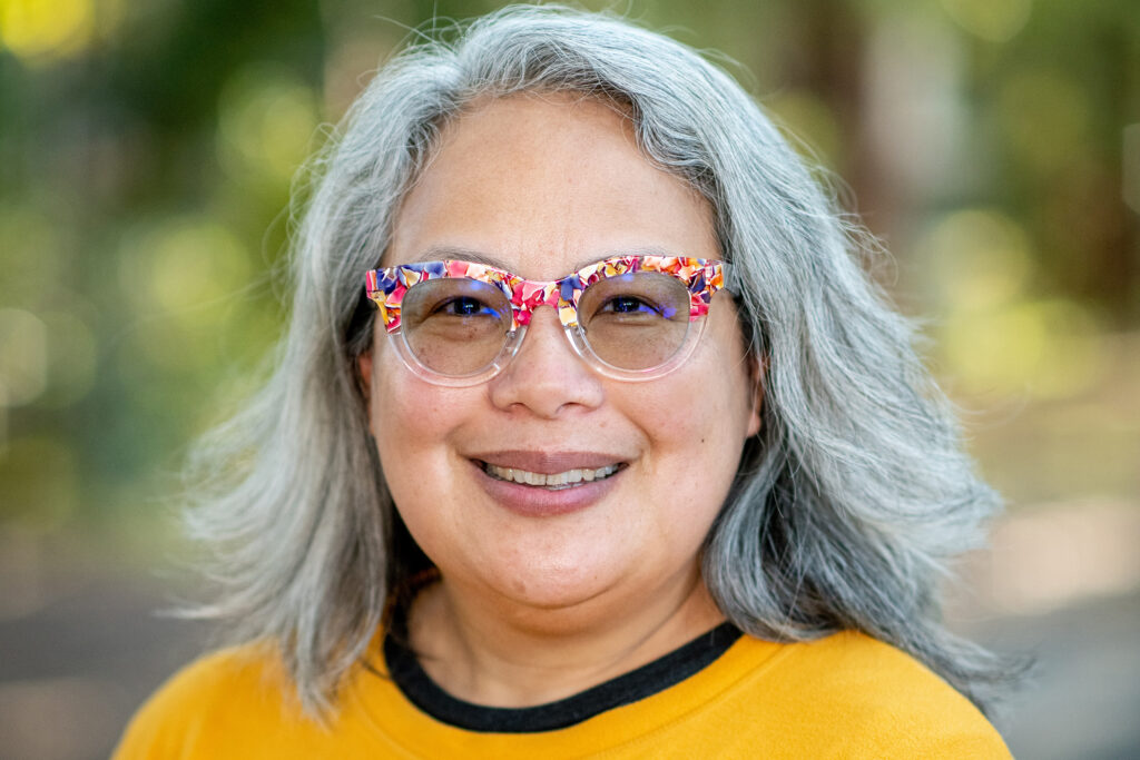 UC Berkeley Professor Abigail De Kosnik smiling in colorful cat-eye glasses and a bright yellow top