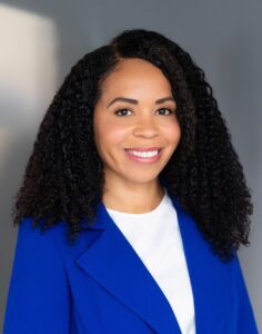 A headshot photo of Professor Aimee J. Carlisle smiling with dark hair in a blue suit jacket.