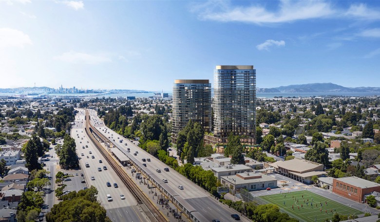 Aerial view of modern high-rise buildings beside a busy highway, with a sports field and distant city skyline under a clear blue sky.