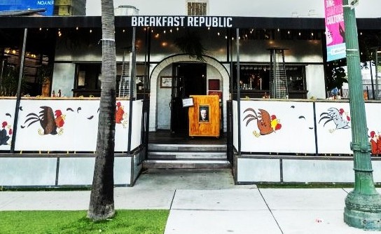 The facade of a building, with fencing around a patio that shows paintings of a roostr and a chicken. A sign atop the building reads "Breakfast Republic."