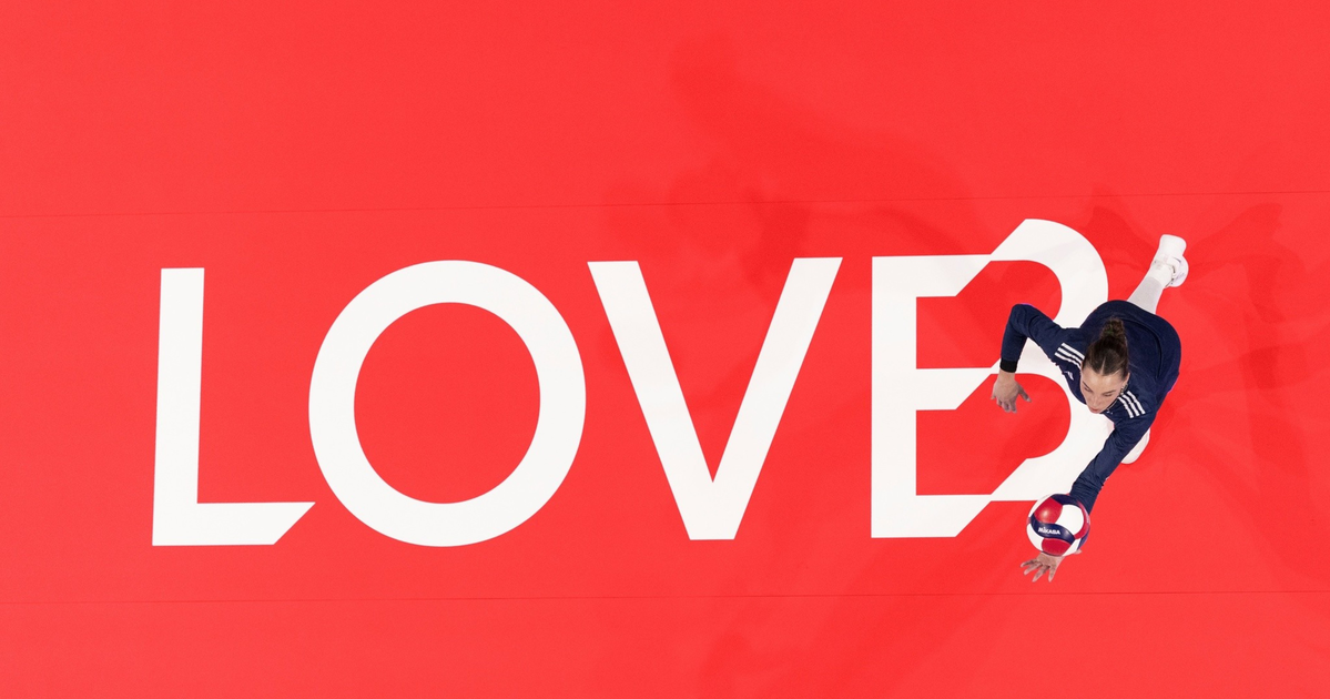 A volleyball player in navy sportswear leaps to hit a ball over a red court with the word "LOVE?" painted in large white letters.