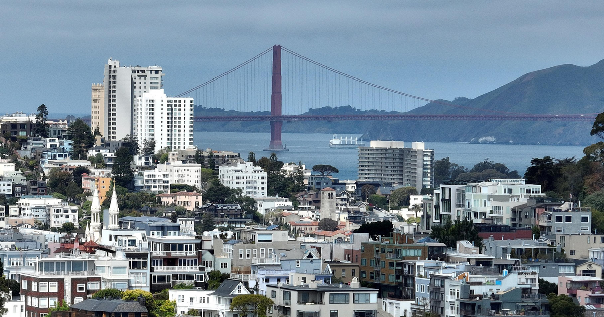 A dense urban area with various residential buildings, hills in the background, and the Golden Gate Bridge spanning across a blue body of water.