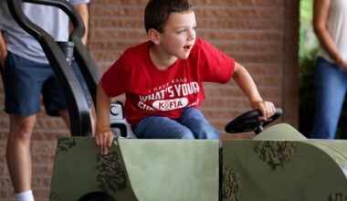 Beau Bewarder sits in his custom-built camouflage ride-on toy car, leaning forward with excitement as he grips the steering wheel.